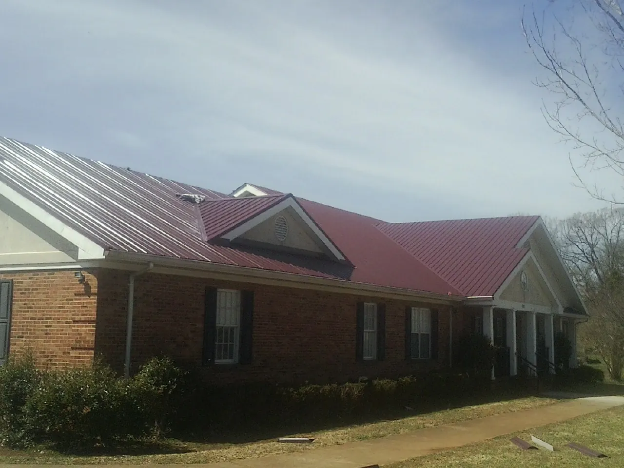Red metal roof with gabled entries on a long brick building, from a Hail Damage Roof Repair job in Orefield