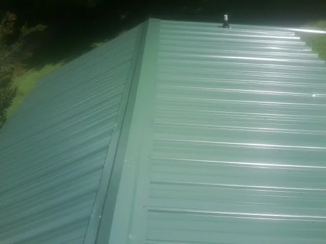New green metal panels meeting at the ridge of a roof — Flat Roof Repair work by our crew in Orefield