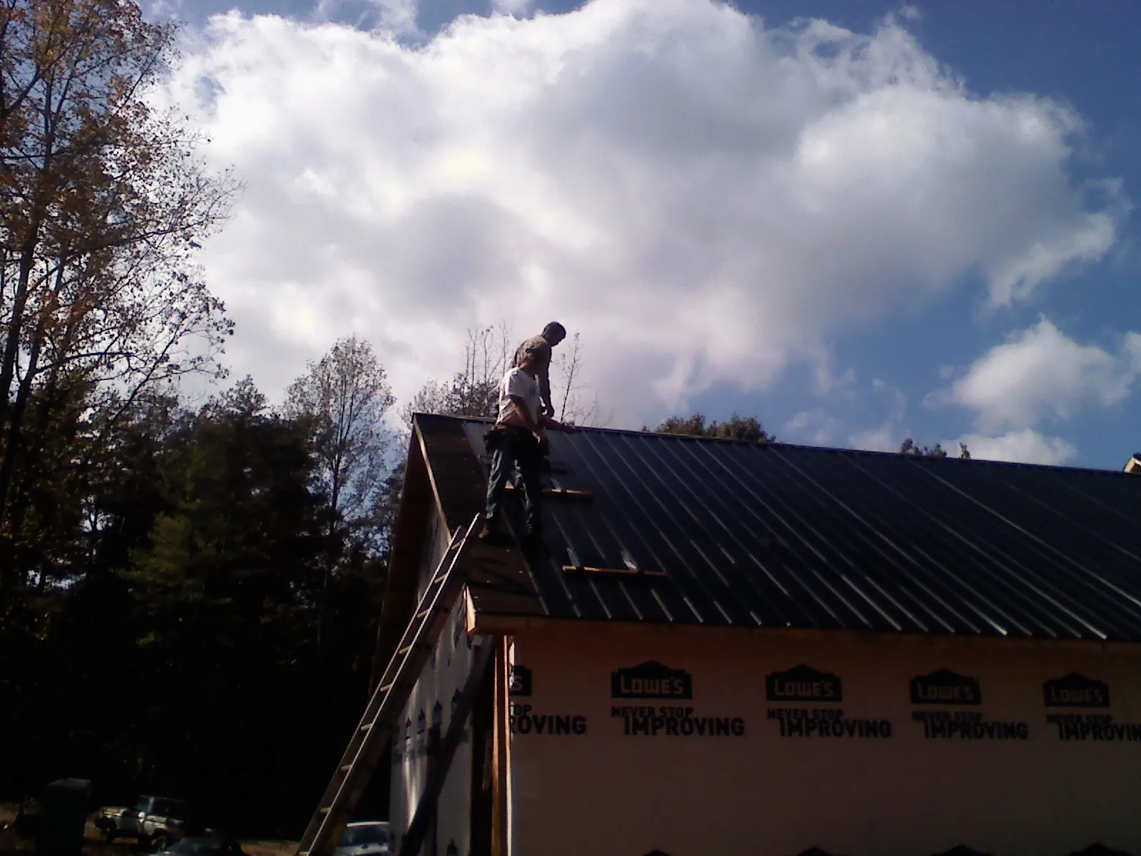Roofer fastening dark metal panels high against a cloudy sky, from a Roof Inspection job in Orefield