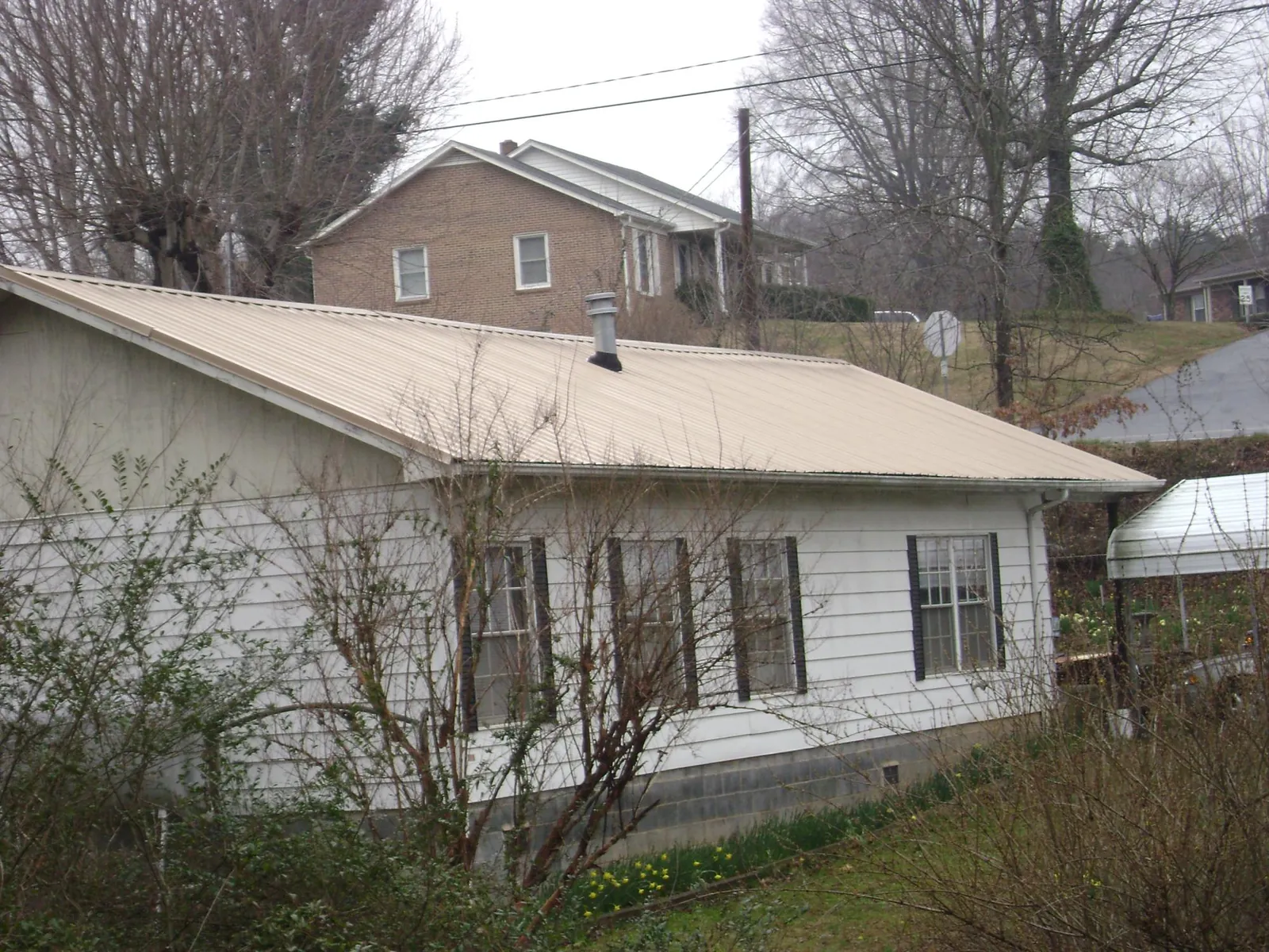 Tan metal roof on a white sided house set into a hillside — Commercial Roofing by Roofing Brothers in Orefield